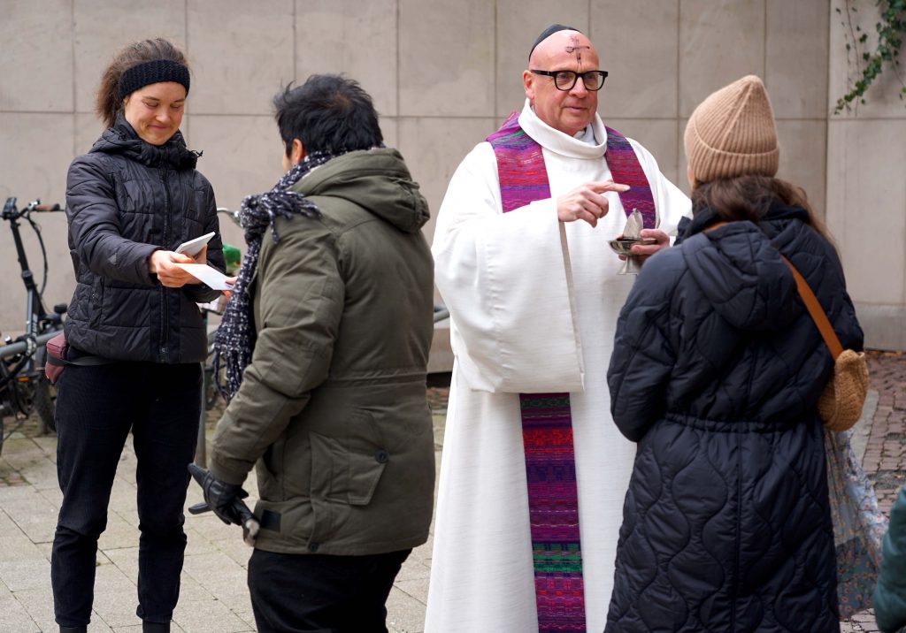Pastor Stefan Tausch verteilte auf dem Platz von Hiroschima das Aschekreuz unter freiem Himmel. Thale Schmitz (links) vom Katholischen Forum gab den Besucherinnen und Besuchern eine Karte mit einer Losung für die Fastenzeit. Foto: Michael Bodin / Katholische Pressestelle Dortmund
