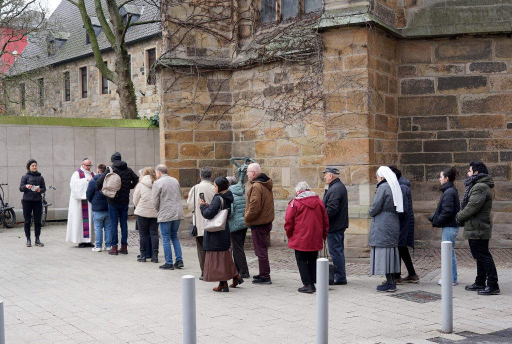 Eine lange Schlange bildete sich auf dem Platz von Hiroschima als Pastor Stefan Tausch dort am Aschermittwoch das Aschekreuz unter freiem Himmel verteilte. Thale Schmitz (links) vom Katholischen Forum gab den Besucherinnen und Besuchern eine Karte mit einer Losung für die Fastenzeit. Foto: Michael Bodin / Katholische Pressestelle Dortmund